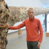 蔡国强站在装置作品《桉树》前，布里斯班现代美术馆，澳洲，2013年。陈昱羽摄，蔡工作室提供。